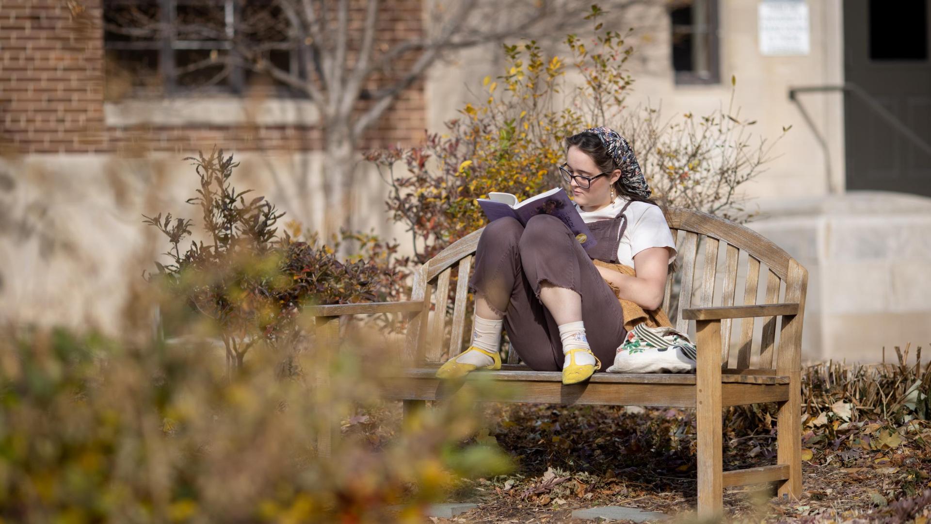 Hamline student sitting on bench outside, reading