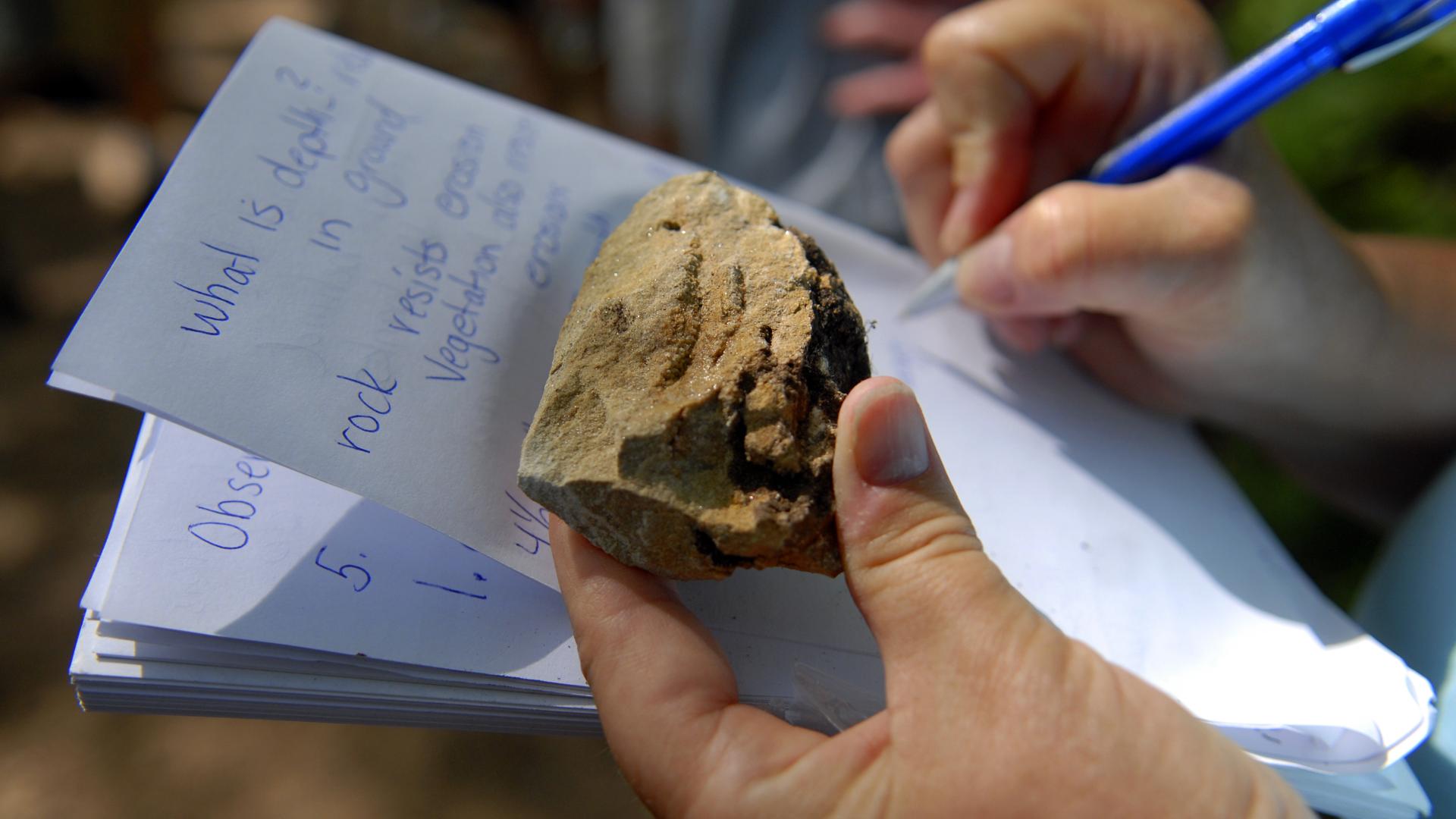 Hands holding rock and notebook in outdoor classroom