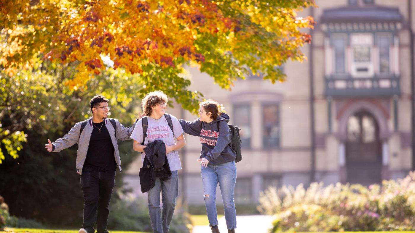 Three students walking in front of Old Main in fall