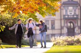 Three students walking in front of Old Main in fall