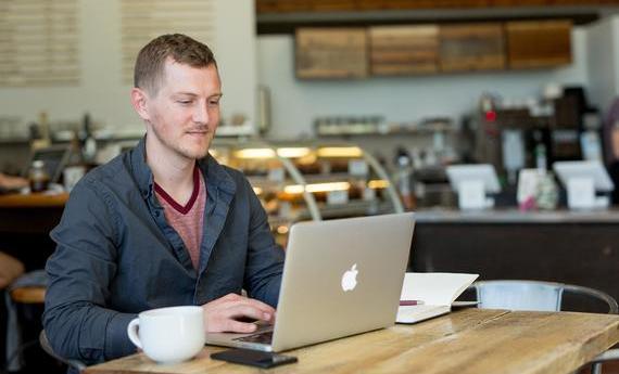 A guest at the Hamline Starbucks sitting at a table with a coffee cup, a laptop, and an open book