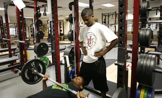 A Hamline student lifting a weight in a gym facility while another Hamline student stands and spots