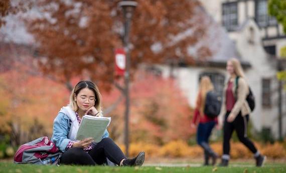 International undergrad student on campus reading a notebook.