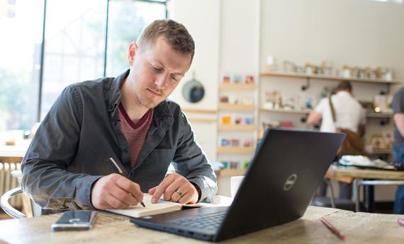 A photo of a working professional working on their laptop at a coffee shop