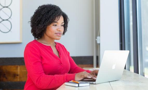 a person sitting and typing on a laptop with a notebook next to them