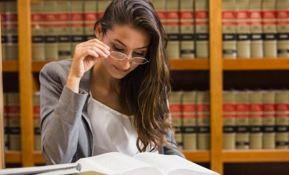 A person sitting reading a book at a table in front of a bookshelf