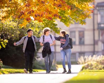 Three students walking in front of Old Main in fall