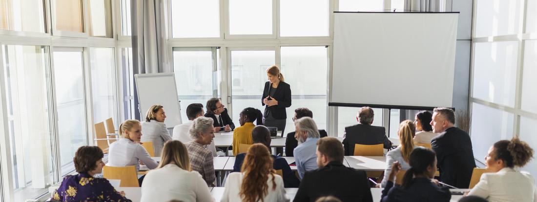 Group of people sitting in lecture with a woman standing in the front of the room