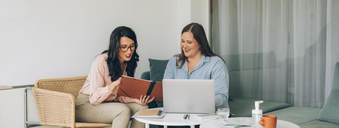 Two women talking with each other sitting in a sofa lokking to a laptop 