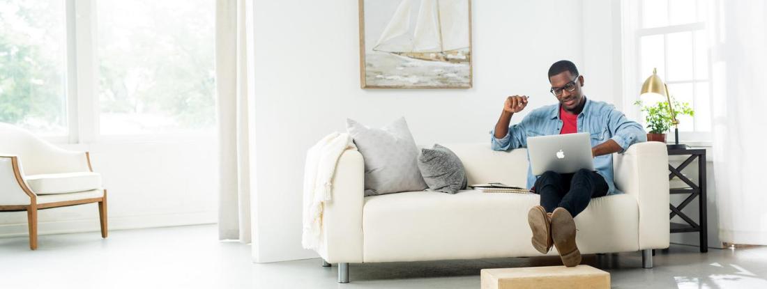 A person sitting on a couch in a white living room working with a laptop on their lap