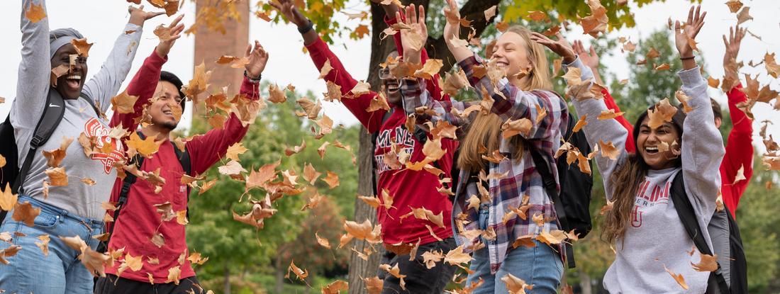 Students throwing fall leaves into the air on Hamline's campus