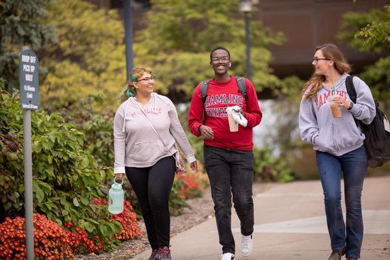 Three Hamline students walking and talking outside on campus in the fall